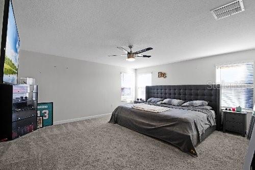 carpeted bedroom with ceiling fan and a textured ceiling