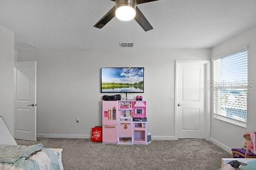 game room with ceiling fan, light carpet, and a textured ceiling