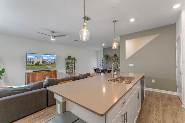 kitchen featuring sink, dishwasher, an island with sink, pendant lighting, and white cabinets