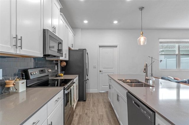 kitchen featuring tasteful backsplash, white cabinetry, sink, hanging light fixtures, and stainless steel appliances