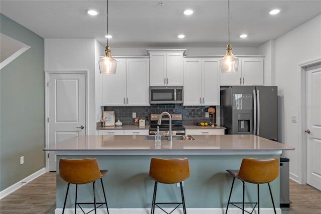 kitchen with stainless steel appliances, an island with sink, hanging light fixtures, and white cabinets