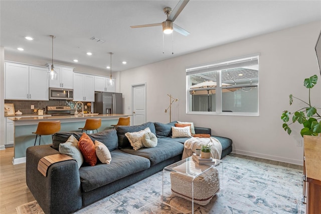 living room featuring ceiling fan, sink, and light wood-type flooring