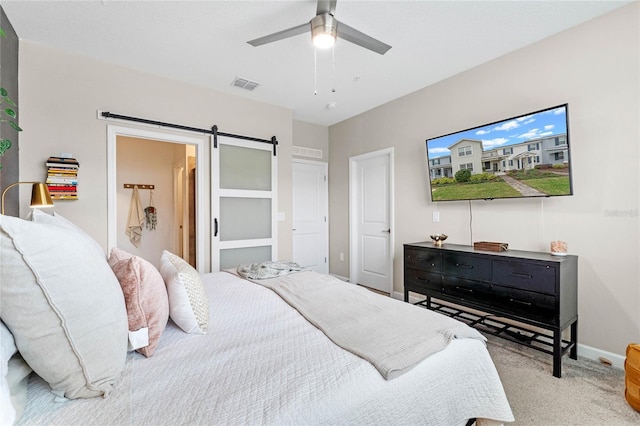 carpeted bedroom with a barn door and ceiling fan