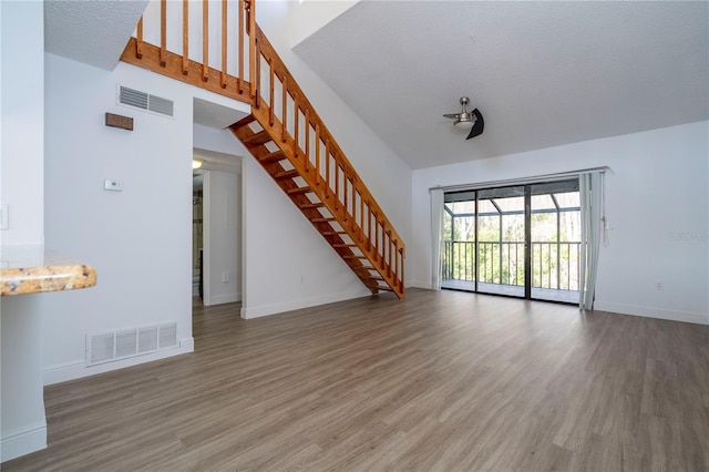 unfurnished living room with hardwood / wood-style flooring, a textured ceiling, and a high ceiling