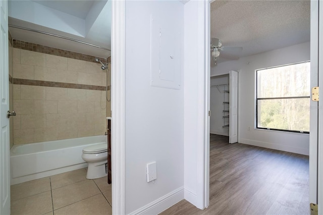 bathroom featuring tiled shower / bath, tile patterned flooring, ceiling fan, toilet, and a textured ceiling