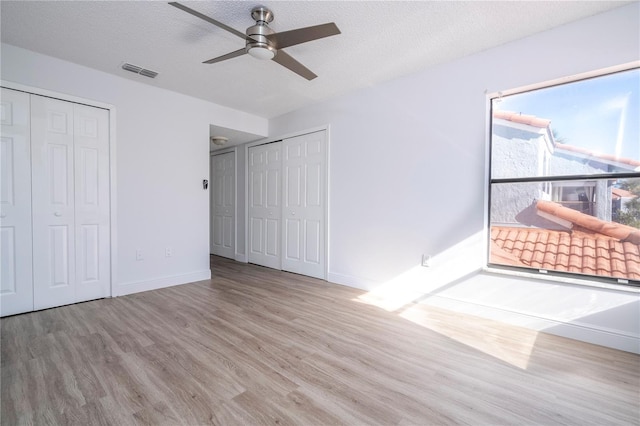 unfurnished bedroom with multiple closets, ceiling fan, a textured ceiling, and light wood-type flooring