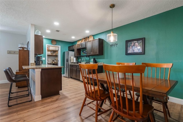 kitchen with pendant lighting, stainless steel fridge with ice dispenser, light wood-style floors, dark brown cabinetry, and baseboards