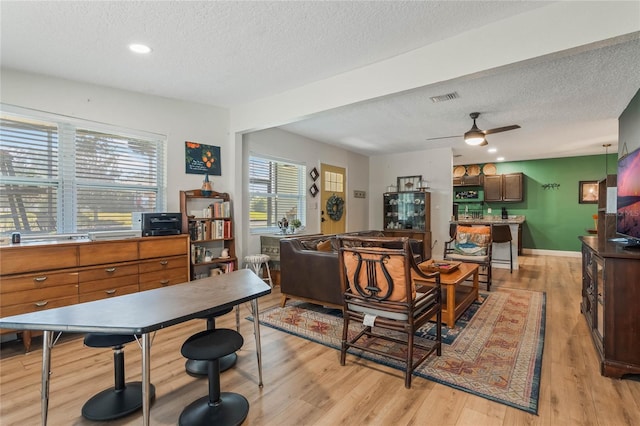 interior space featuring a ceiling fan, visible vents, a textured ceiling, and light wood finished floors