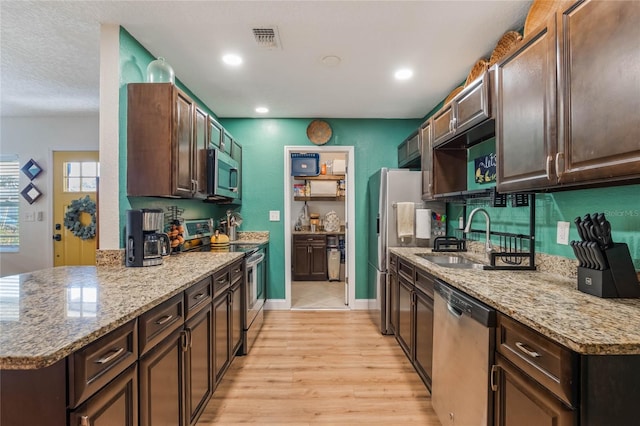 kitchen featuring stainless steel appliances, a sink, visible vents, dark brown cabinets, and light stone countertops