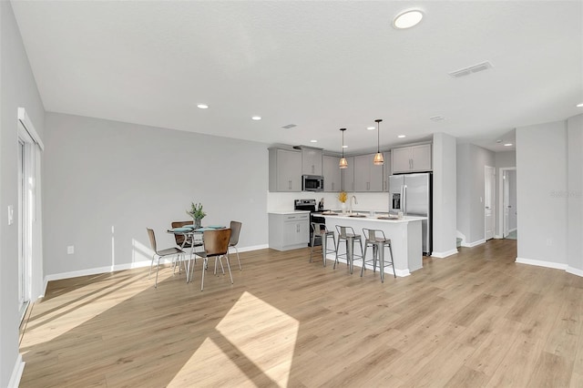 kitchen featuring pendant lighting, a breakfast bar area, gray cabinetry, stainless steel appliances, and an island with sink