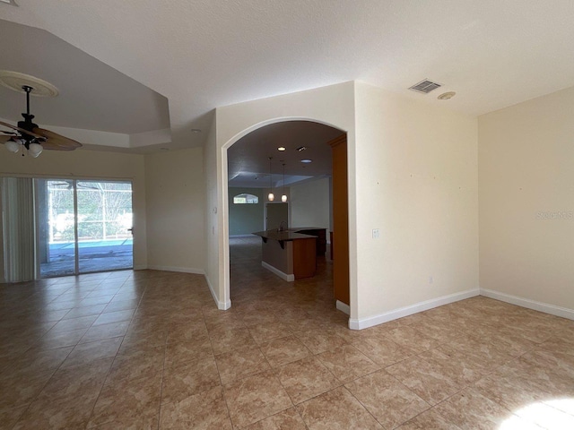 spare room featuring arched walkways, a raised ceiling, visible vents, a ceiling fan, and baseboards