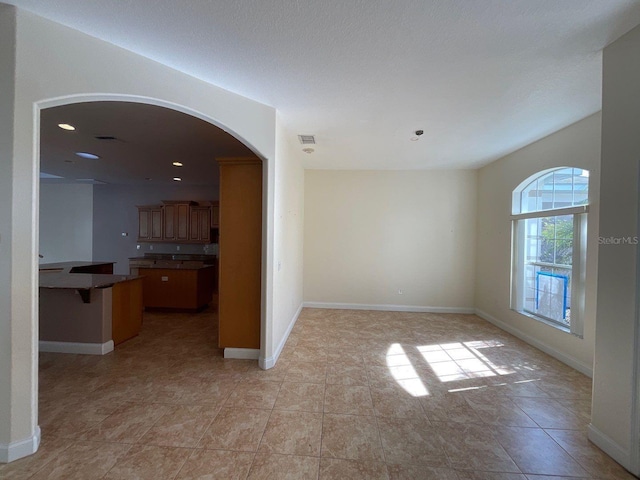 empty room with arched walkways, visible vents, baseboards, and recessed lighting