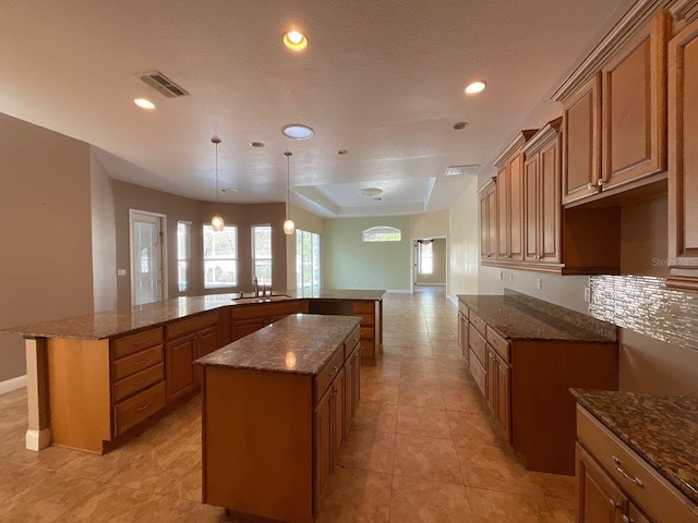 kitchen with sink, hanging light fixtures, kitchen peninsula, a kitchen island, and dark stone counters