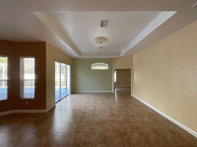 tiled spare room featuring a raised ceiling, visible vents, and baseboards