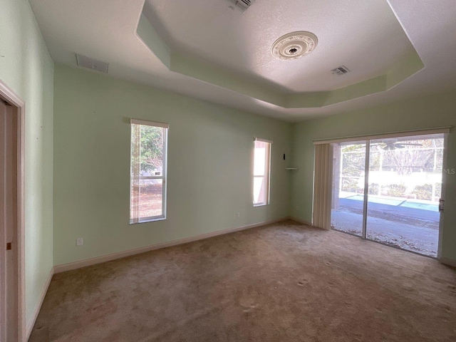 carpeted empty room featuring visible vents, a tray ceiling, and baseboards