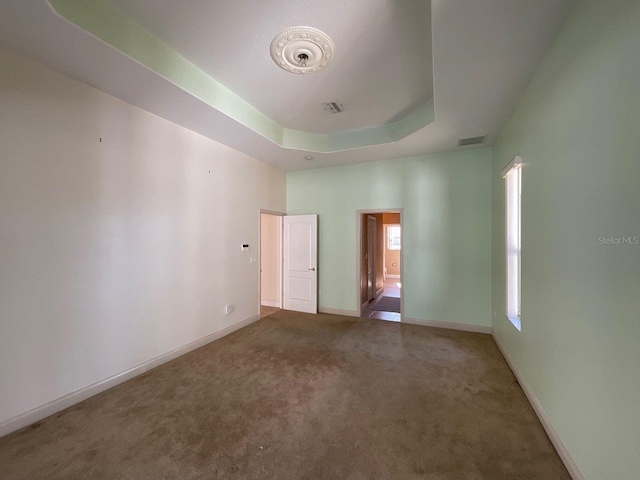 unfurnished bedroom with carpet floors, a tray ceiling, visible vents, and baseboards