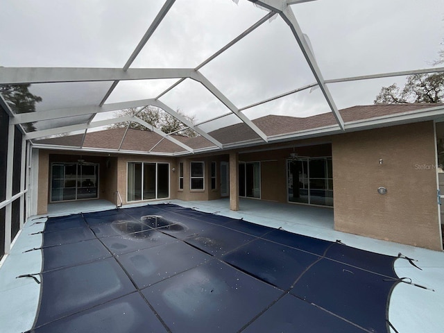 rear view of house with roof with shingles, a patio, stucco siding, a ceiling fan, and glass enclosure