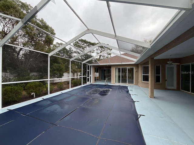 view of swimming pool with glass enclosure, a ceiling fan, and a patio