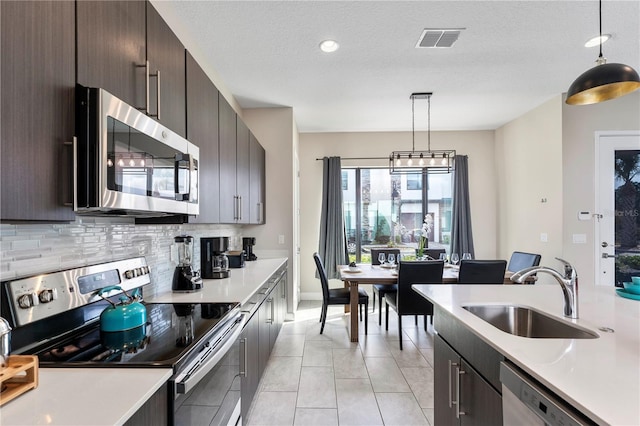 kitchen featuring dark brown cabinetry, sink, tasteful backsplash, pendant lighting, and stainless steel appliances