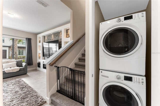 clothes washing area featuring light tile patterned flooring, stacked washing maching and dryer, and a textured ceiling