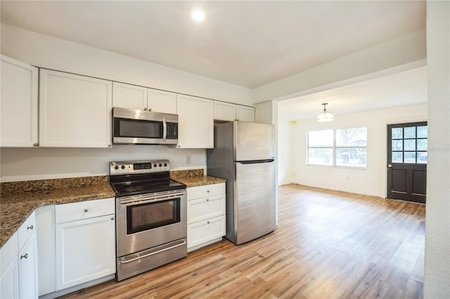 kitchen featuring appliances with stainless steel finishes, white cabinetry, light hardwood / wood-style floors, decorative light fixtures, and dark stone counters