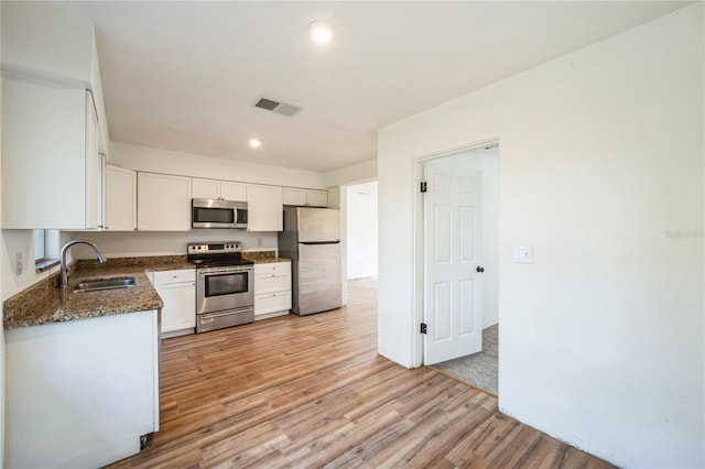 kitchen featuring sink, white cabinets, dark stone counters, stainless steel appliances, and light hardwood / wood-style flooring