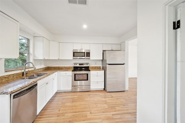 kitchen featuring white cabinetry, sink, dark stone countertops, light hardwood / wood-style floors, and stainless steel appliances