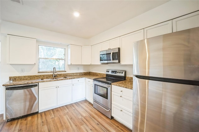 kitchen with sink, white cabinetry, light hardwood / wood-style flooring, dark stone countertops, and appliances with stainless steel finishes