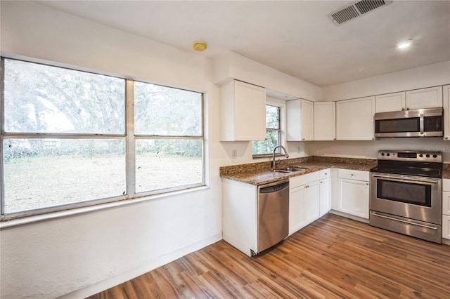 kitchen featuring sink, dark stone countertops, hardwood / wood-style floors, stainless steel appliances, and white cabinets