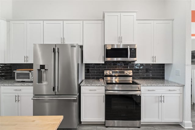 kitchen with stainless steel appliances, white cabinetry, and light stone countertops