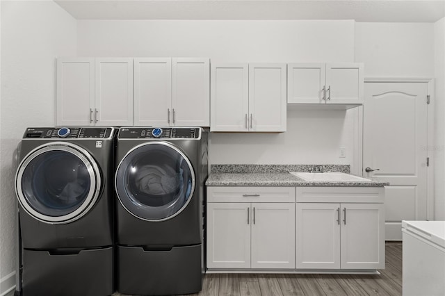 laundry room with cabinets, washing machine and clothes dryer, sink, and light hardwood / wood-style flooring