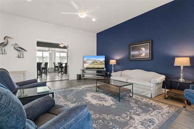 living room with a ceiling fan, vaulted ceiling, wood finished floors, and an accent wall