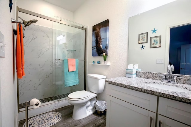 bathroom with a marble finish shower, toilet, vanity, and wood finished floors