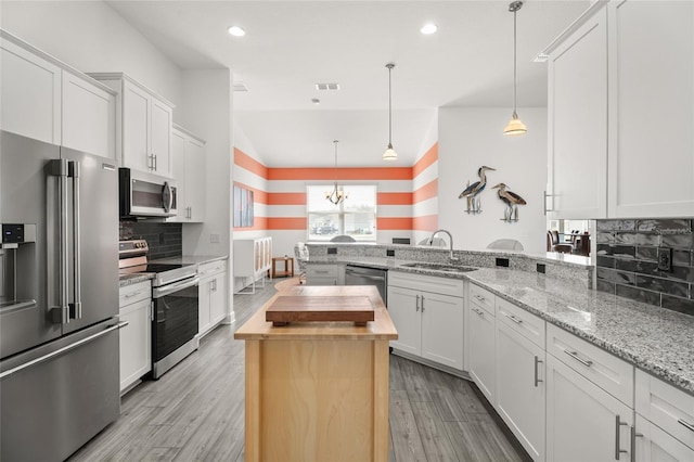 kitchen with light wood-style flooring, a peninsula, a sink, stainless steel appliances, and decorative backsplash