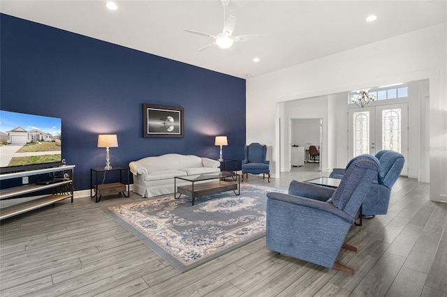 living area with ceiling fan with notable chandelier, an accent wall, recessed lighting, wood finished floors, and baseboards
