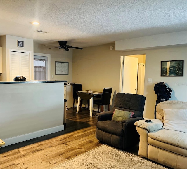 living room with wood-type flooring, ceiling fan, and a textured ceiling