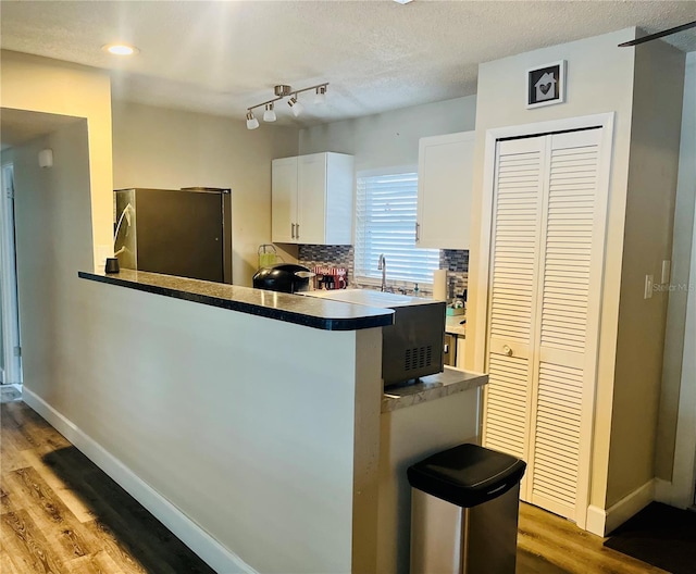 kitchen with hardwood / wood-style flooring, stainless steel refrigerator, white cabinets, decorative backsplash, and kitchen peninsula