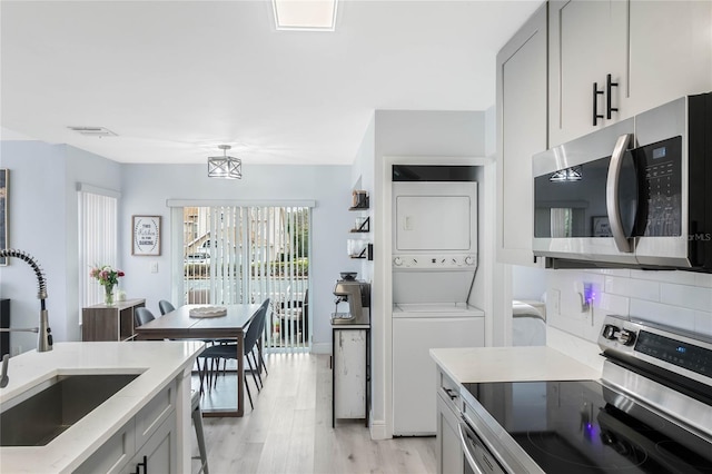 kitchen with stacked washer / drying machine, sink, gray cabinetry, stainless steel appliances, and light hardwood / wood-style floors