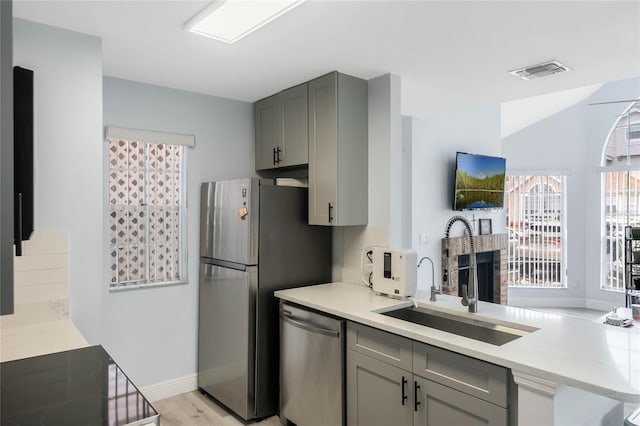 kitchen with sink, light hardwood / wood-style flooring, gray cabinets, backsplash, and stainless steel appliances