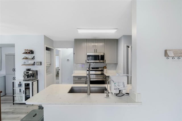 kitchen featuring gray cabinetry, light stone counters, appliances with stainless steel finishes, stacked washer / dryer, and backsplash