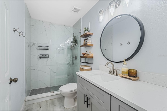 bathroom featuring hardwood / wood-style flooring, tiled shower, vanity, and toilet