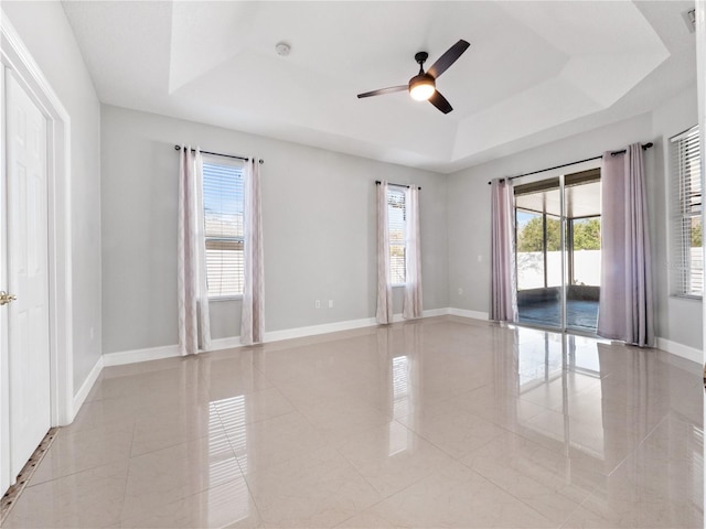 spare room with ceiling fan, a tray ceiling, and light tile patterned floors