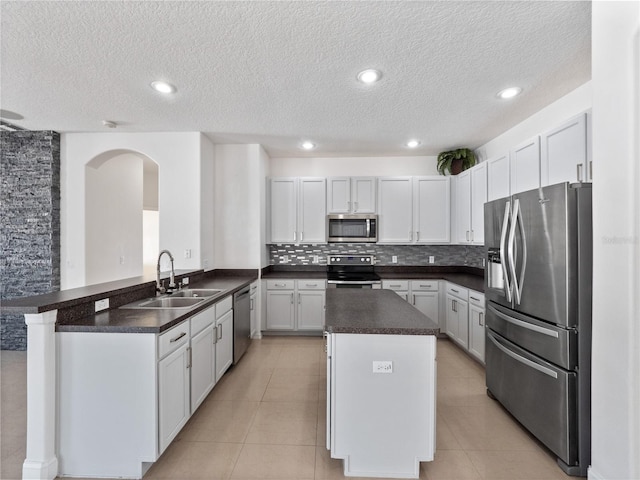 kitchen featuring sink, light tile patterned floors, kitchen peninsula, stainless steel appliances, and white cabinets