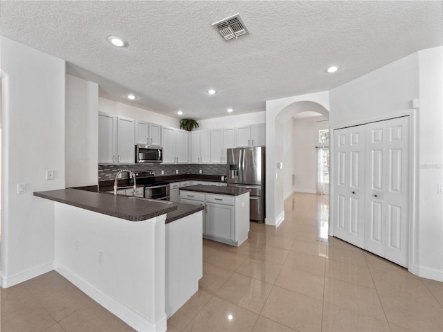 kitchen with light tile patterned floors, appliances with stainless steel finishes, white cabinets, decorative backsplash, and kitchen peninsula