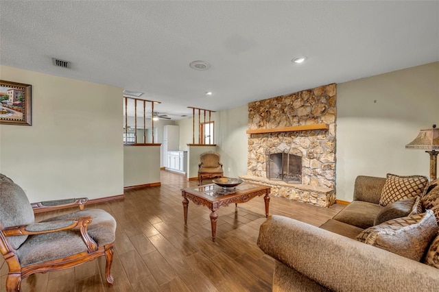 living room with ceiling fan, a fireplace, hardwood / wood-style floors, and a textured ceiling