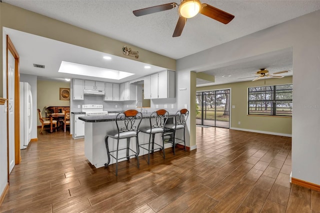 kitchen with white cabinetry, white appliances, kitchen peninsula, and dark wood-type flooring