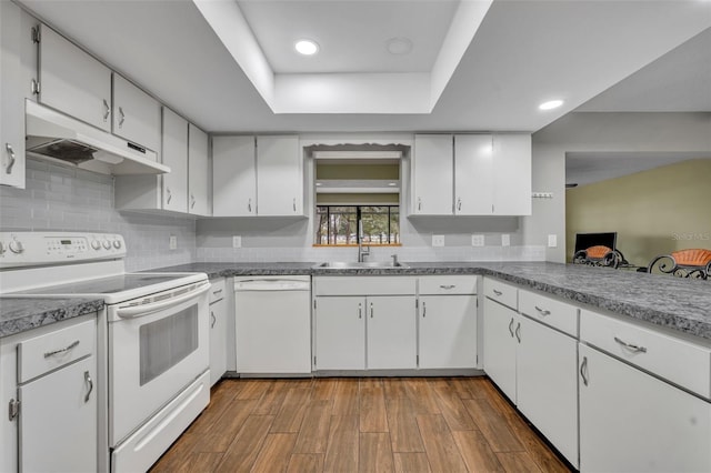 kitchen featuring white appliances, white cabinetry, hardwood / wood-style floors, backsplash, and a raised ceiling