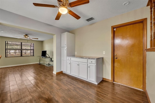 interior space with ceiling fan, a textured ceiling, dark hardwood / wood-style floors, and white cabinets