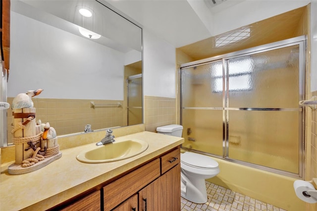 full bathroom featuring vanity, toilet, combined bath / shower with glass door, and tile walls