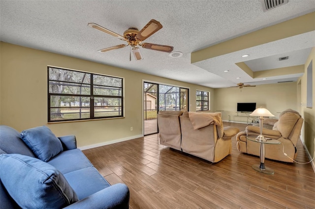 living room with hardwood / wood-style flooring, a raised ceiling, a textured ceiling, and ceiling fan